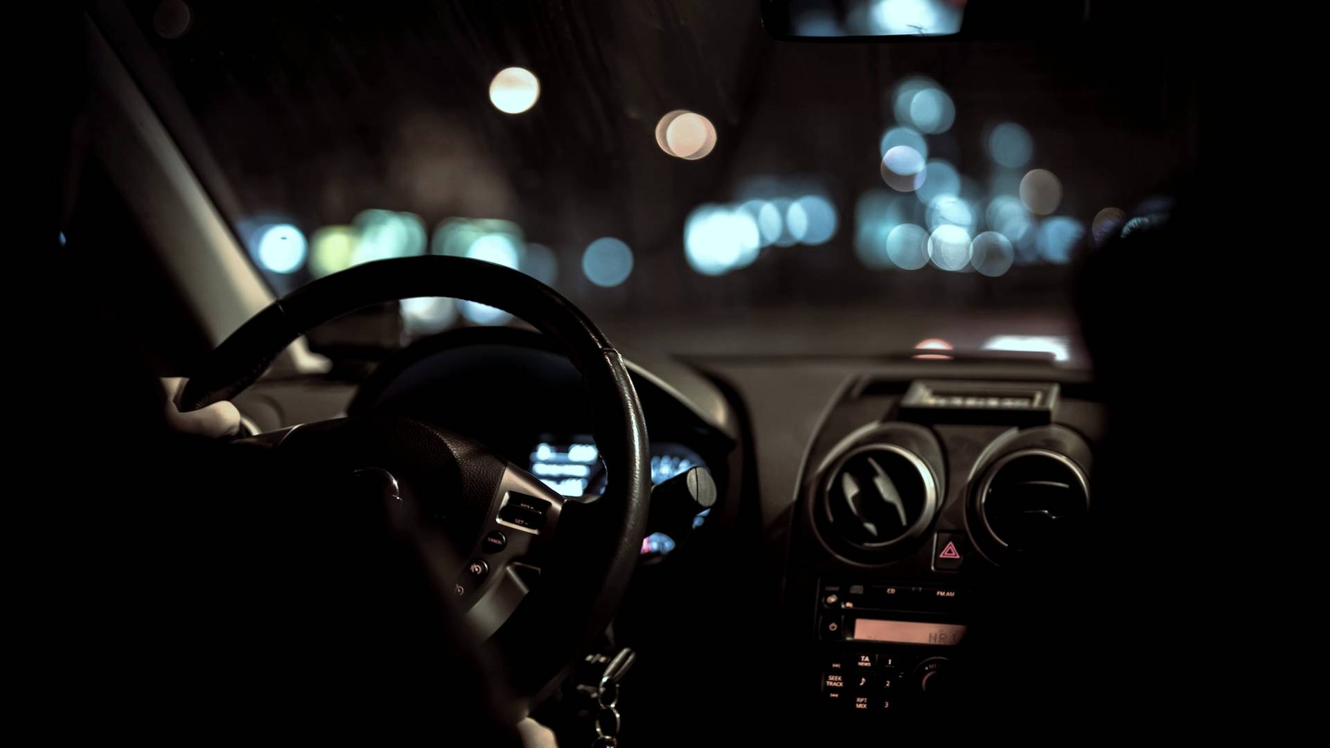 Vue de l’intérieur d’une voiture la nuit, depuis la place du passager arrière : le volant, le tableau de bord et les lumières floues de la ville derrière le pare-brise