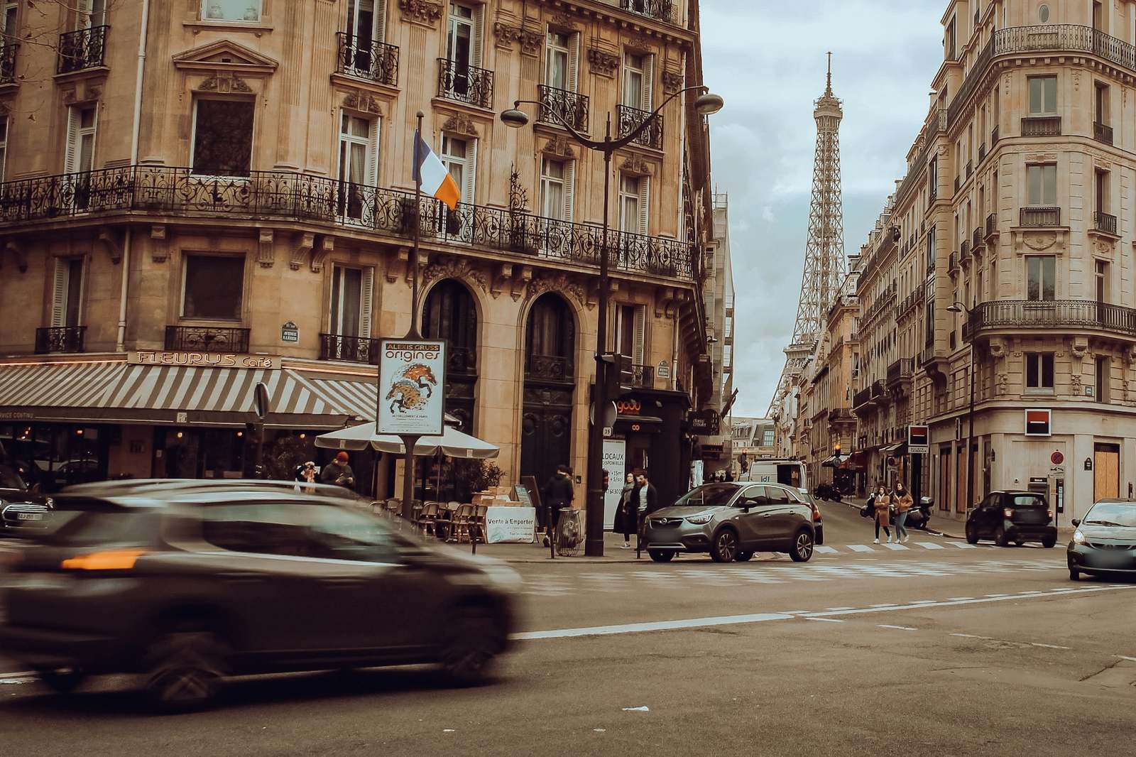 Une rue haussmannienne de Paris, une voiture en mouvement au premier plan et la tour Eiffel au fond
